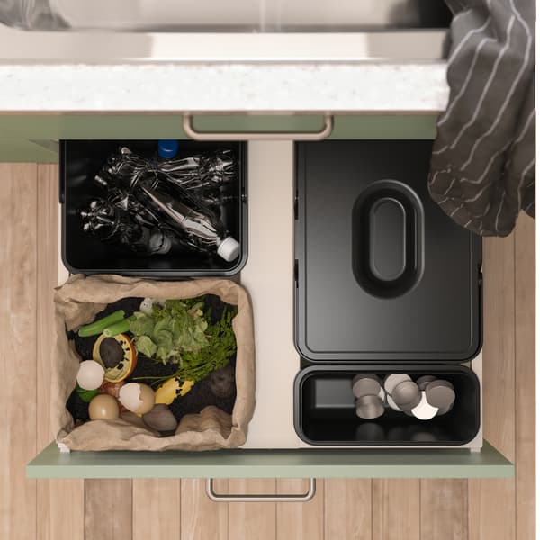 Seen from above is an open kitchen drawer with black waste sorting bins inside. Different kinds of waste is sorted in them.