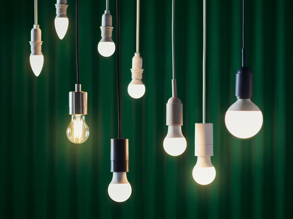 Seis bombillas LED de distintos diseños colgadas a diferentes alturas sobre el fondo de una cortina verde oscura.