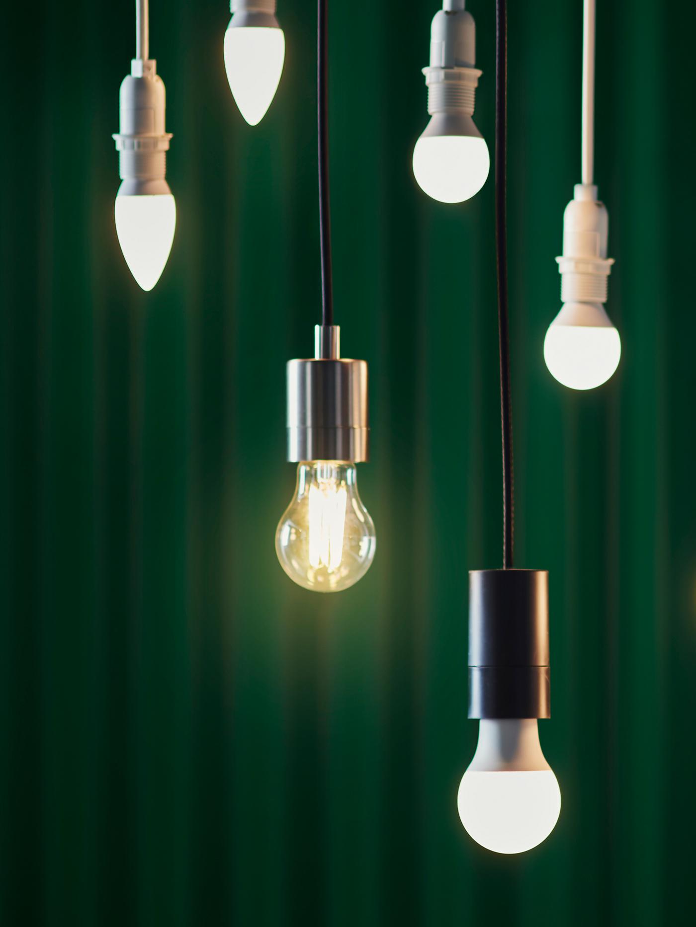 Seis bombillas LED de distintos diseños colgadas a diferentes alturas frente a una cortina verde oscura.