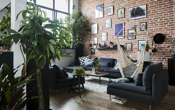 Séjour au plafond haut, mur en briques et canapé modulable gris.