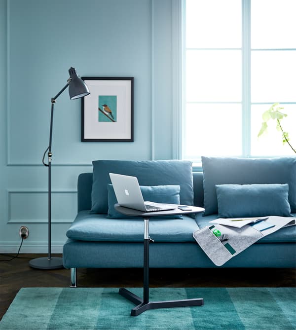 Séjour avec canapé, lampadaire, organiseur mural à suspendre et support réglable pour portable, créant un bureau-canapé efficace