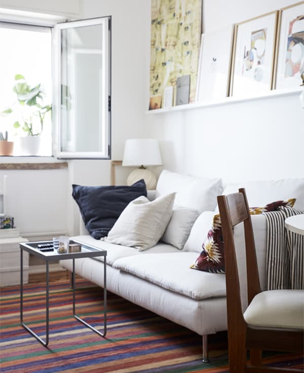 Séjour avec murs blancs, canapé blanc et tapis aux motifs colorés.