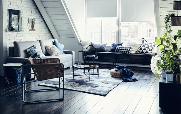 Séjour monochrome avec toit en pente, canapé gris, fauteuil en rotin et grand tapis texturé.