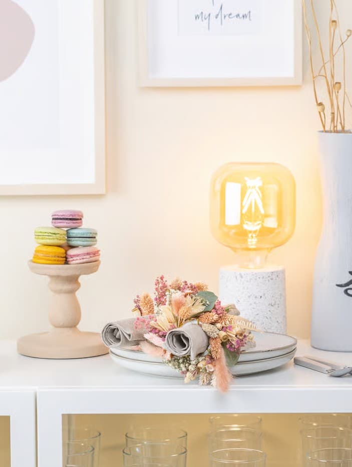 Selbstgebastelte Boho-Serviettenringe aus Kunstblumen liegen auf einen Tellerstapel