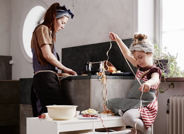 Seorang ibu sedang mencuci pinggan mangkuk di dapur sementara anak perempuan kecilnya membuat kalungan.