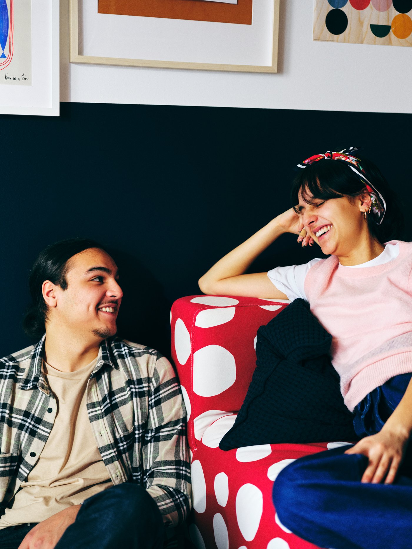 Seorang lelaki dan wanita tersenyum pada satu sama lain, seorang duduk di atas sofa dua tempat duduk KLIPPAN berwarna merah dan putih, seorang lagi di atas lantai di sebelahnya.