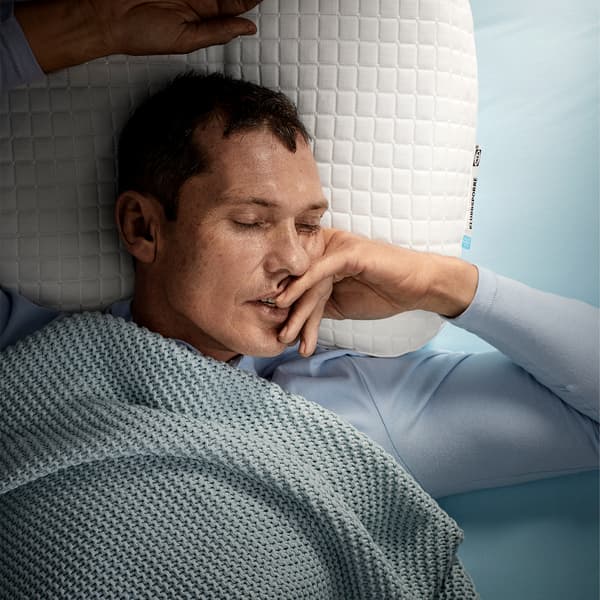 Seorang lelaki yang baring telentang, sedang tidur nyenyak di atas bantal ergonomik KLUBBSPORRE IKEA.