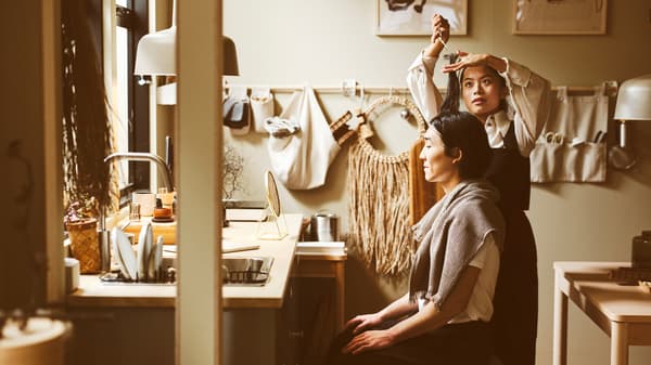 Seorang yang berdiri sedang memotong rambut seorang yang duduk di dapur yang mempunyai permukaan kerja EKBACKEN kesan kayu ash.