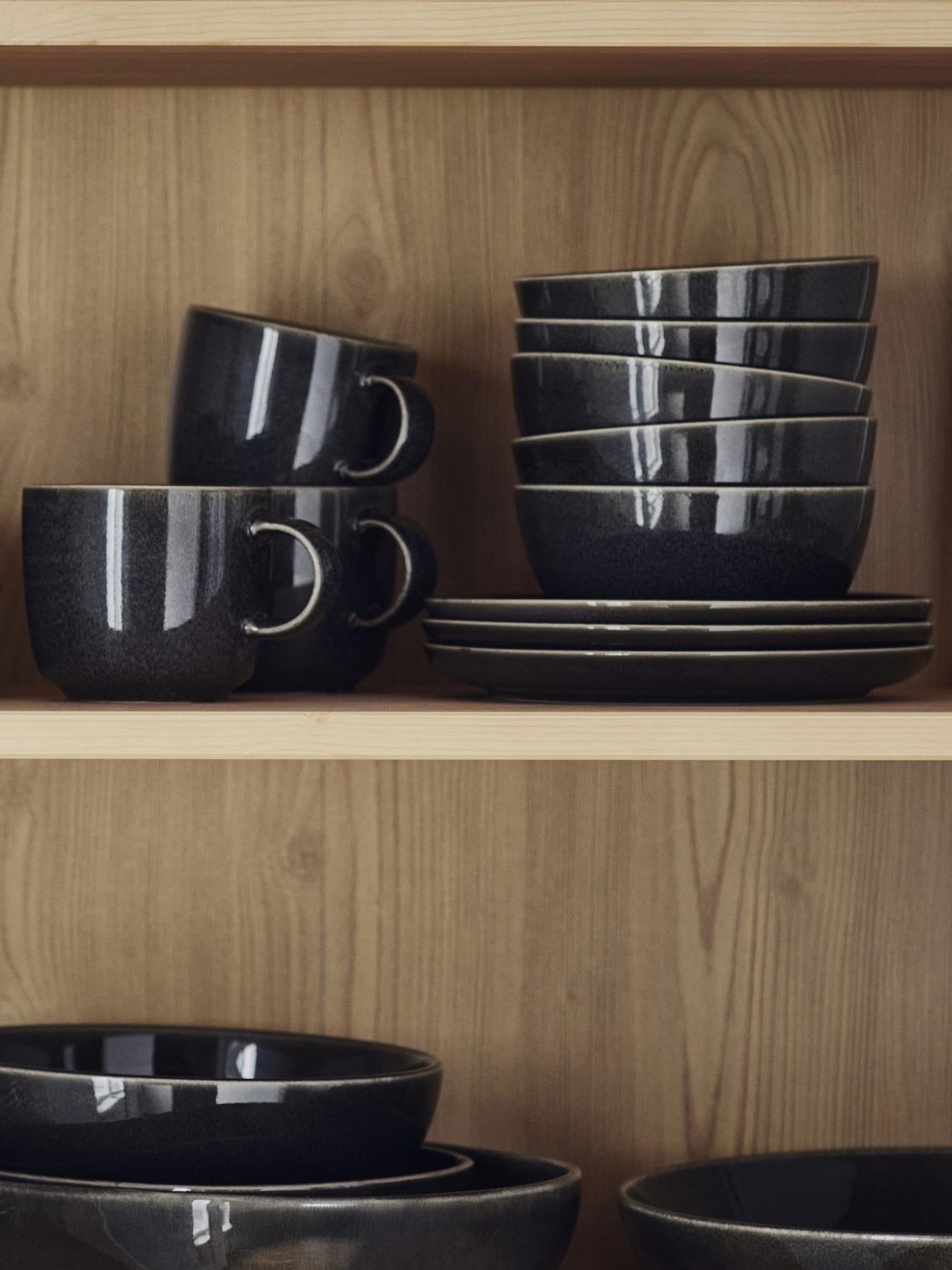 Seria zastawy stołowej GlADELIG w kolorze ciemnoszarym stoi na półce na drewnianym regale.