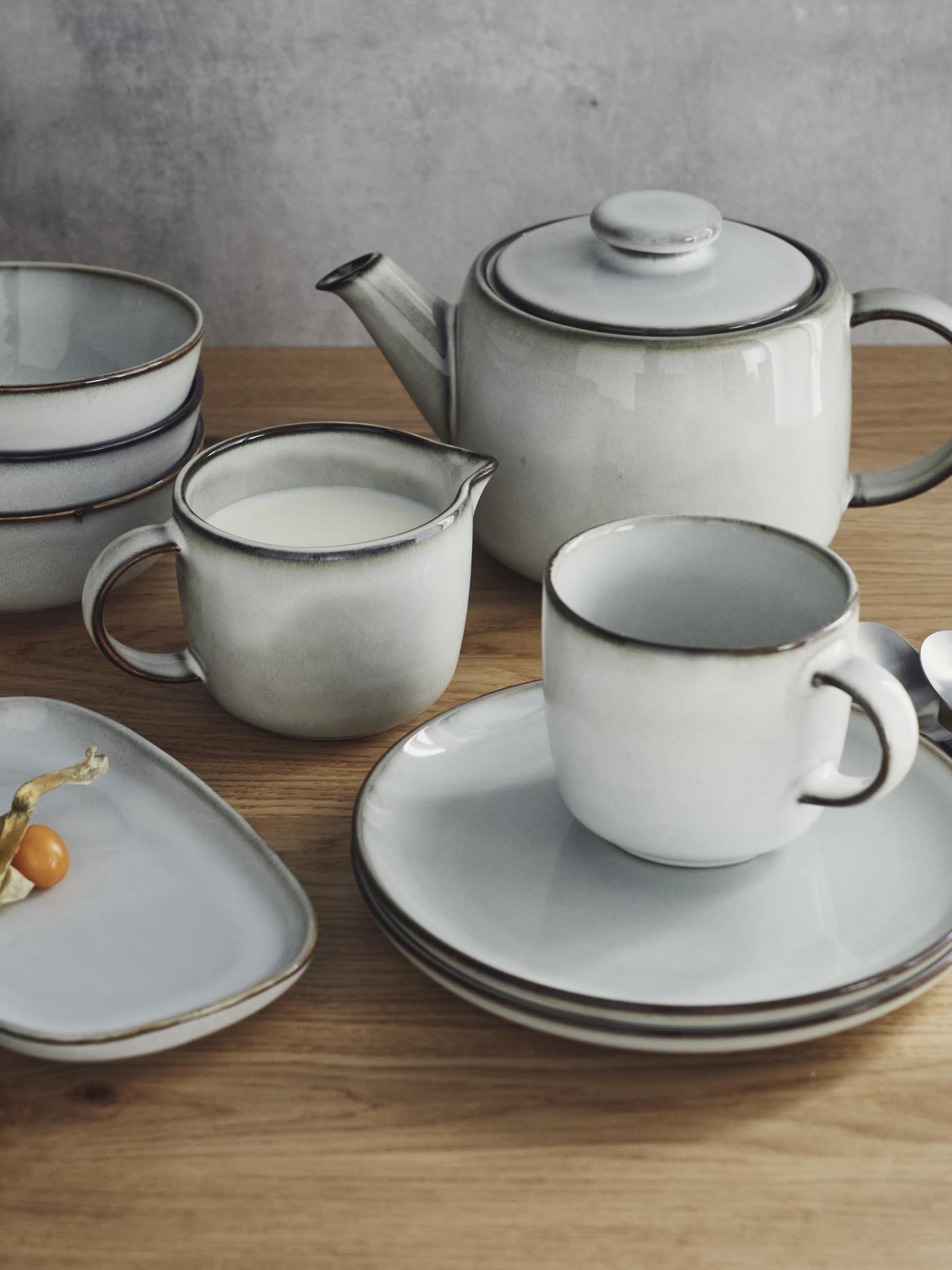 Seria zastawy stołowej GlADELIG w kolorze jasnoszarym stoi na drewnianym blacie.