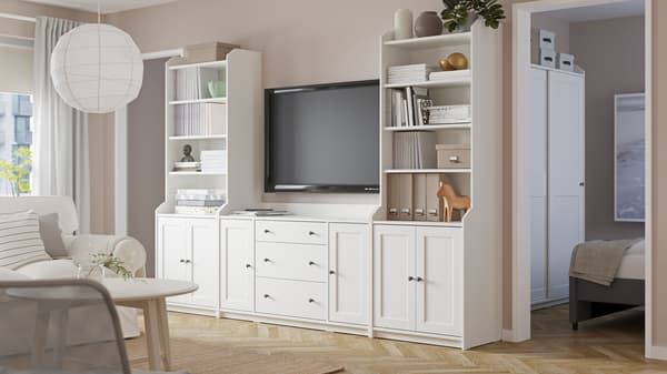 Serie de muebles de almacenamiento HAUGA en tonos blancos con puertas y repisas rodeando un televisor.