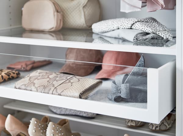 Sertarele cu depozitare KOMPLEMENT de la IKEA cu fronturi din sticlă, în care sunt depozitate portofele, pălării și accesorii. 