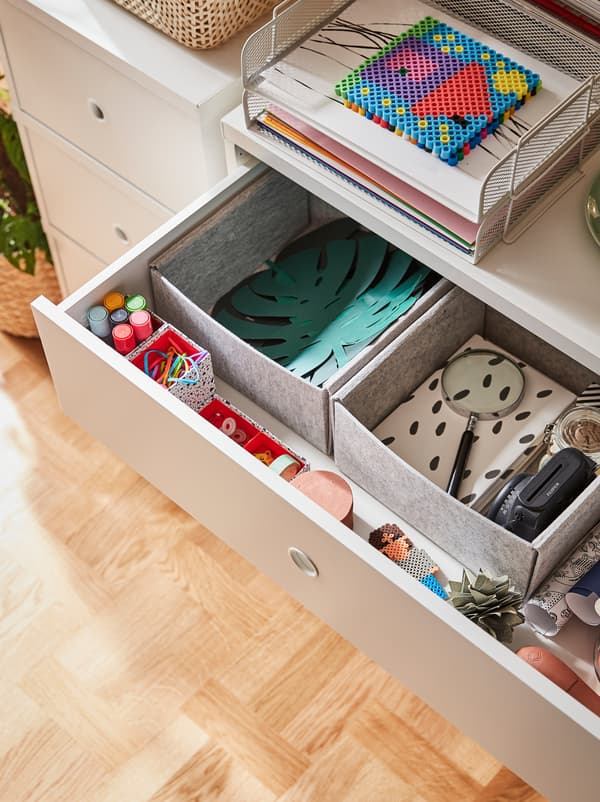 Sertarul superior al unei comode este deschis și dezvăluie hârtie și accesorii pentru desen organizate în cutii KOMPLEMENT.