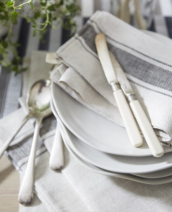 Serviettes en coton de couleur neutre et couverts sur une pile d’assiettes blanches.