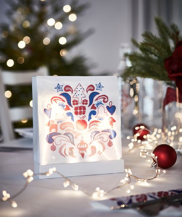 Serviettes en papier à motif festif dans un support éclairé, qui contribue au décor de la table de fête.
