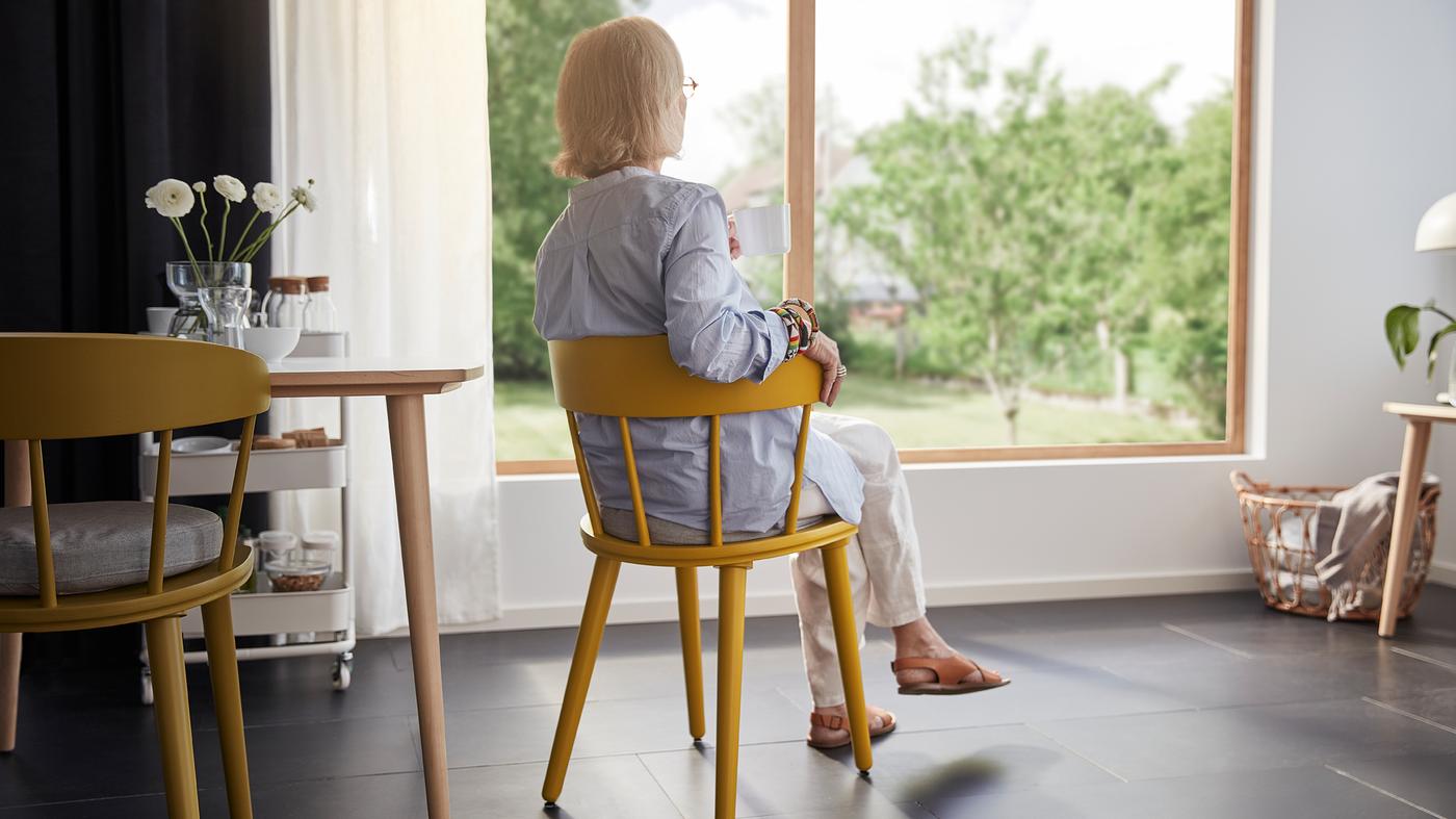 Šesťdesiatnička je pohodlne usadená na stoličke OMTÄNKSAM. Je otočená chrbtom a pozerá sa z okna v obývacej izbe.