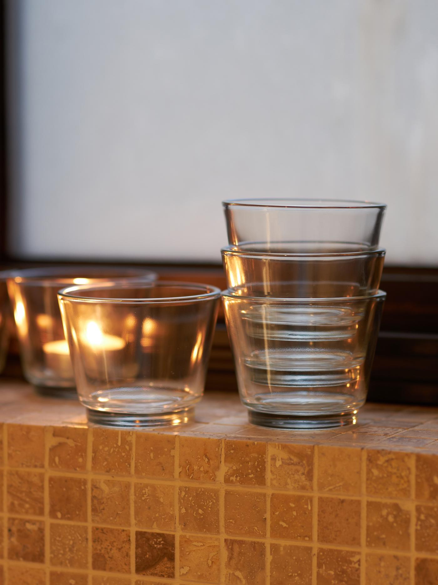 Set of glass GALEJ candleholders placed on a bathroom wall ledge with a candle lit in the background.
