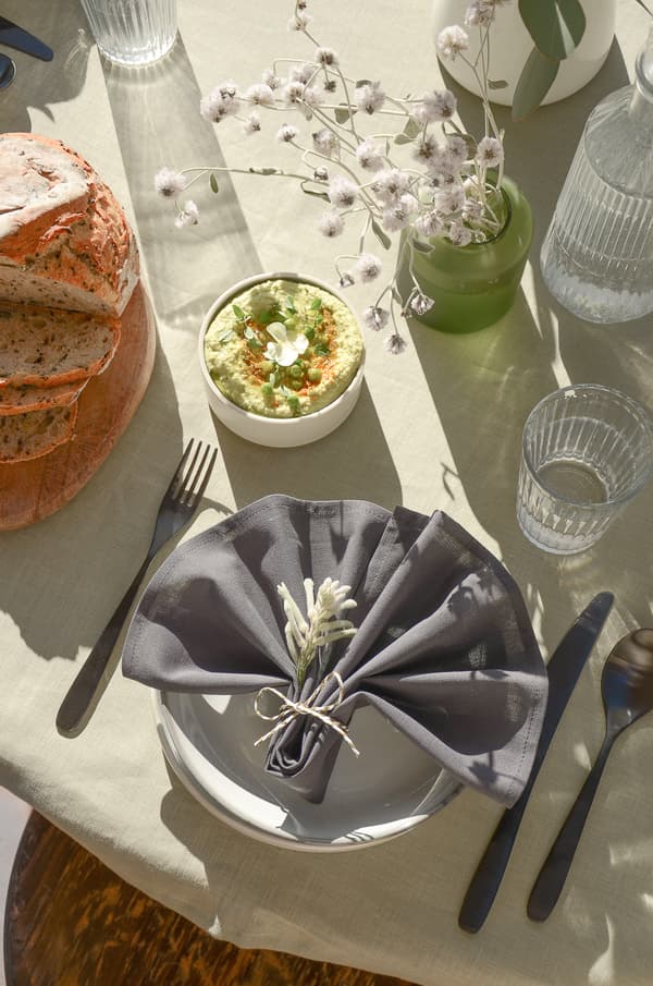 Set table with bread, dip, gray napkin with flowers, glasses and dried flowers on light tablecloth.