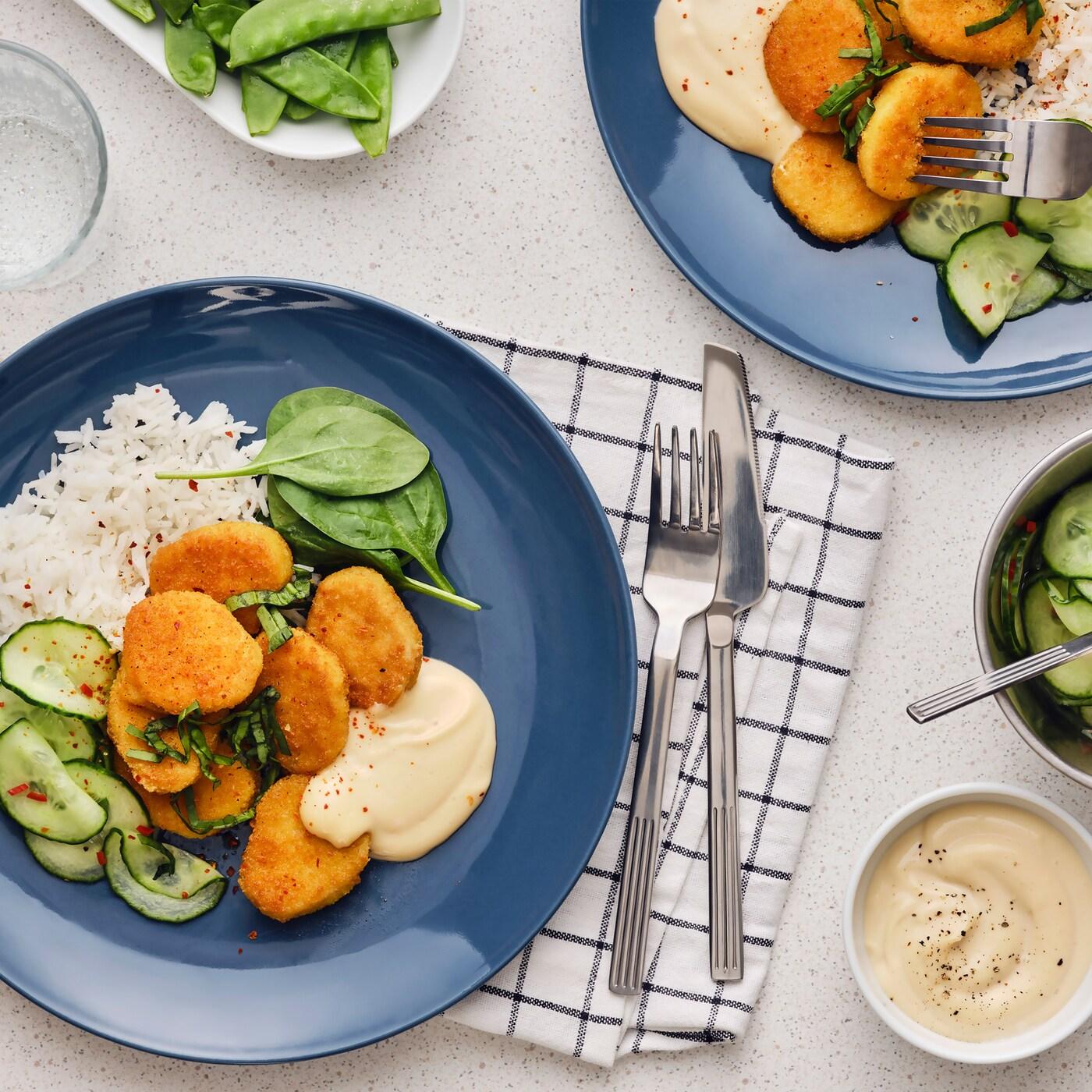 Seven fried wheat-based pieces are served on a blue plate together with rice, a cucumber salad with chili and soy mayonnaise.