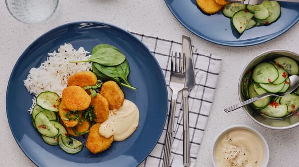 Seven fried wheat-based pieces are served on a blue plate together with rice, a cucumber salad with chili and soy mayonnaise.