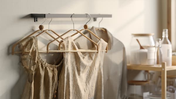 Several bamboo HÖSVANS hangers on a metal wall-mounted rail holding dry beige shirts and dresses beside a table.