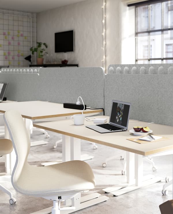 Several beige/white desks and beige/white chairs grouped together and separated with a light grey screen between the desks.