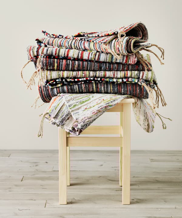 Several colourful TÅNUM rugs stacked on a small stool.