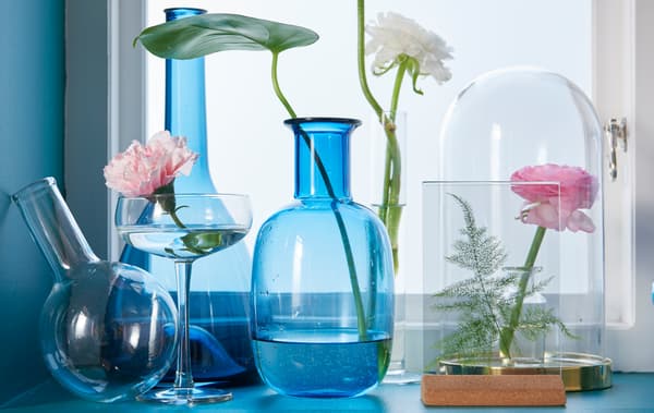 Several different shaped blue and clear glass vases and an IKEA BEGÅVNING glass dome on a window sill.