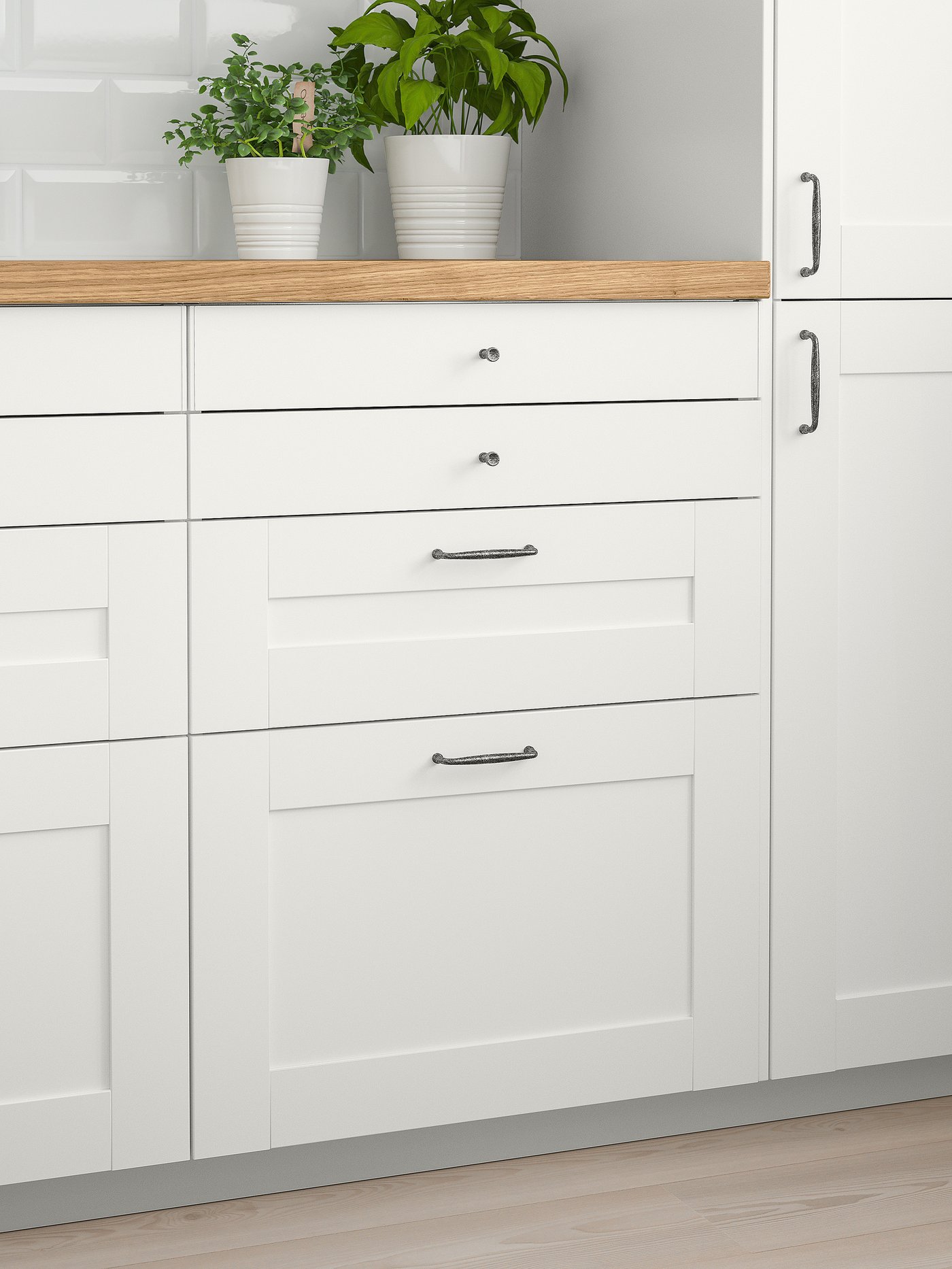 Several drawers with SÄVEDAL white drawer fronts below a wooden worktop. Two white plant pots containing herbs stand on top.