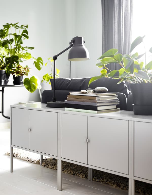 Several IKEA LIXHULT cabinets in metallic grey behind the sofa, with a lamp and some plants and books on top.