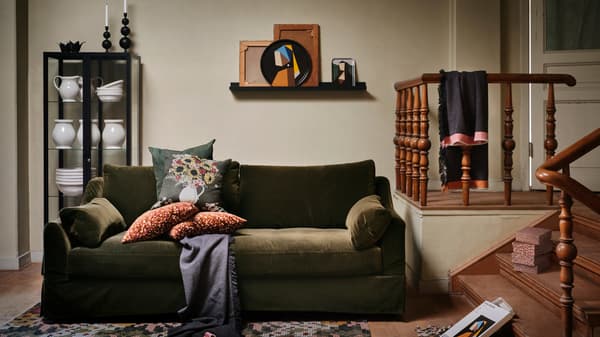 Several items from the IKEA DEKORERA collection stand in a warm living room, with a dark green sofa with cushions.