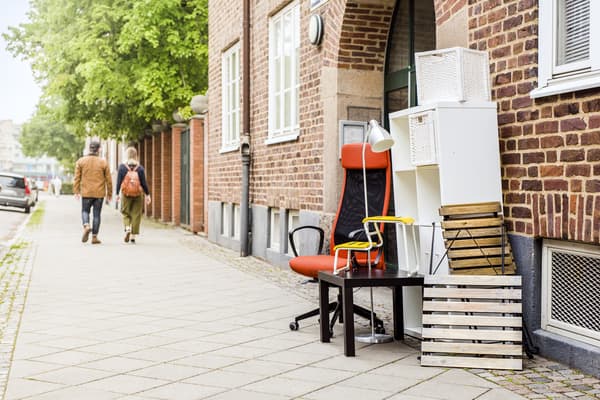 Several items of furniture are lined up in the street in front of a house door ready to be collected.
