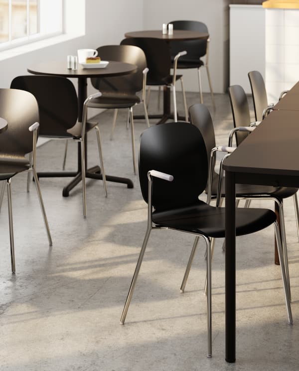 Several large tables with matching chairs and next to it several small round tables with chairs, a white mug and a window.