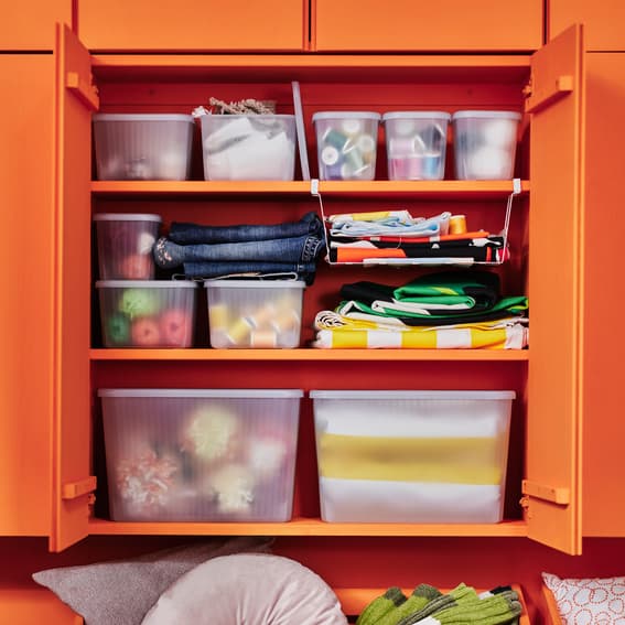 Several RYKTA storage boxes in a bright orange coloured IVAR cabinet with its hinged doors open, showing neatly organised clothes and items. 