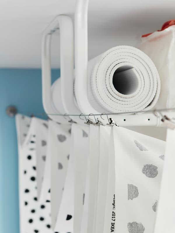 Several white MULIG clothes bars mounted onto the ceiling for storage hidden by a curtain hung between two curtain wires.