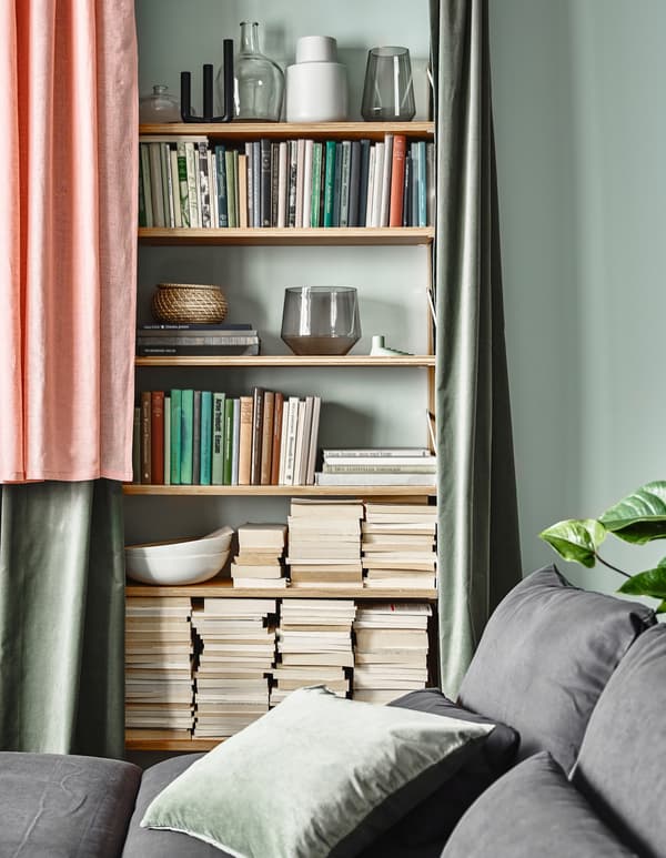 Shelves stacked with books and ornaments partly hidden by some curtains in a living room setting.