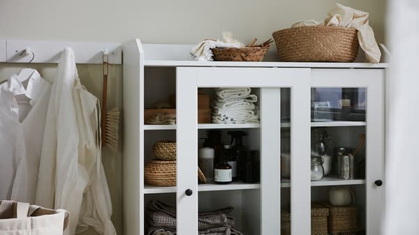 Shirts on hooks, a glass-door cabinet with boxes and a basket in natural materials, folded textiles, and laundry products.