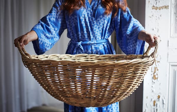 شخص يرتدي كيمونو أزرق منقوش يحمل سلة روطان كبيرة مستديرة.