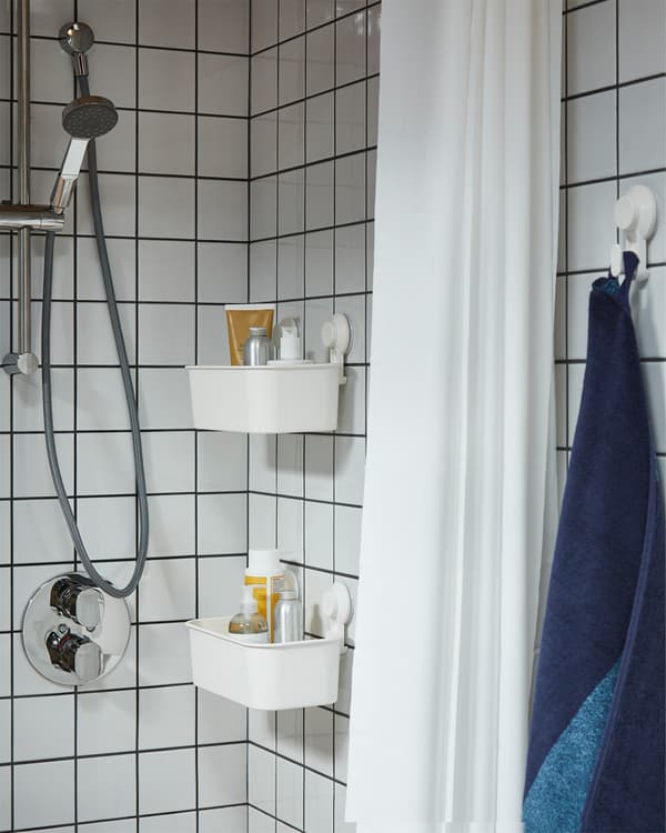 Shower in white tiles, white shower curtain and two white baskets with suction cups that store shampoos and shower gels.