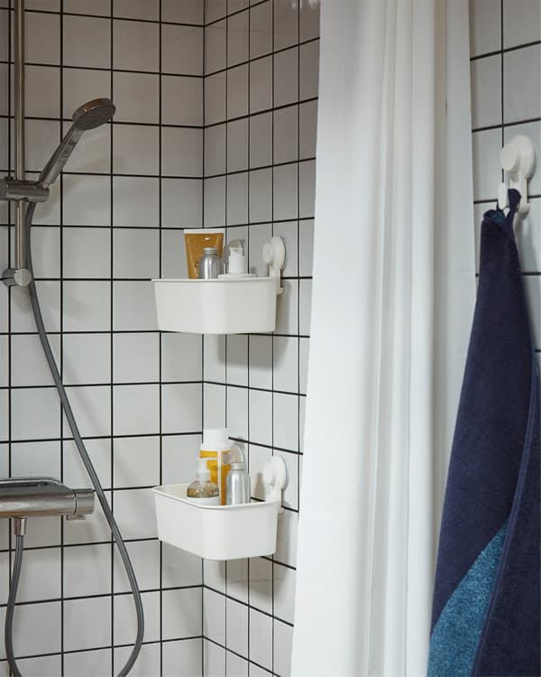 Shower in white tiles, white shower curtain and two white baskets with suction cups that store shampoos and shower gels.
