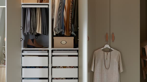 Side-by-side PAX wardrobes with grey-beige REINSVOLL doors. One wardrobe is open, revealing neatly organised contents.