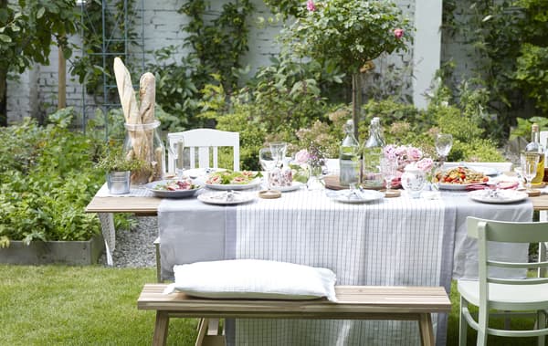 Side view of a long table set for a meal outside in a lush, green garden on a sunny spring day.
