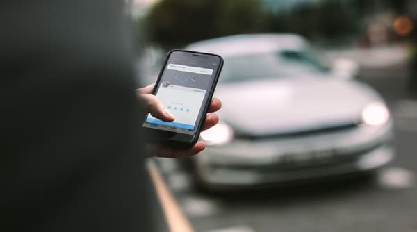 Silhouette of a person with a mobile phone and car in the background. 
