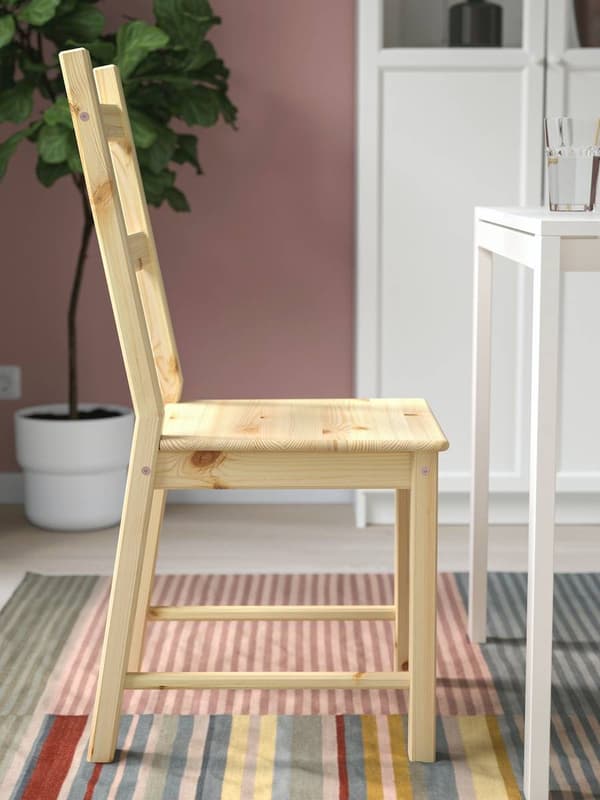 Silla IVAR color madera frente a una mesa blanca y sobre una alfombra de colores.