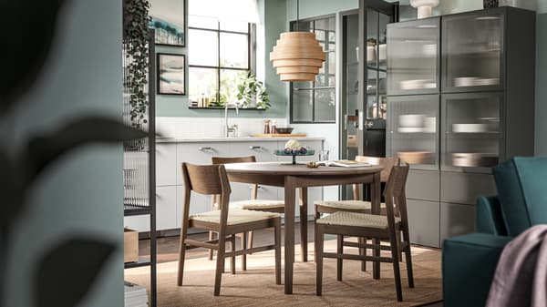 Sillas SKANSNÄS de haya café en una mesa redonda extensible SKANSNÄS de chapa/haya café bajo una lámpara colgante DYKARKLOCKA.
