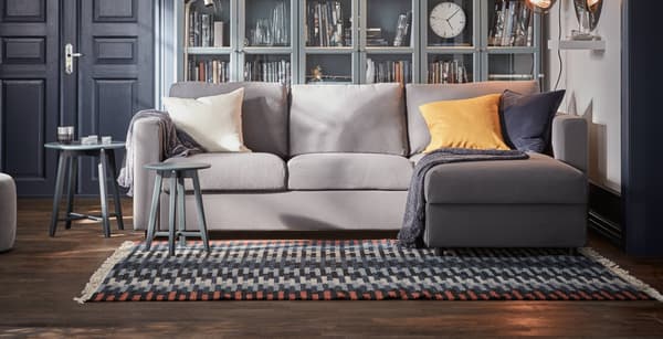 Sillón de tres cuerpos en color gris claro, con cojines sobre el y una manta.