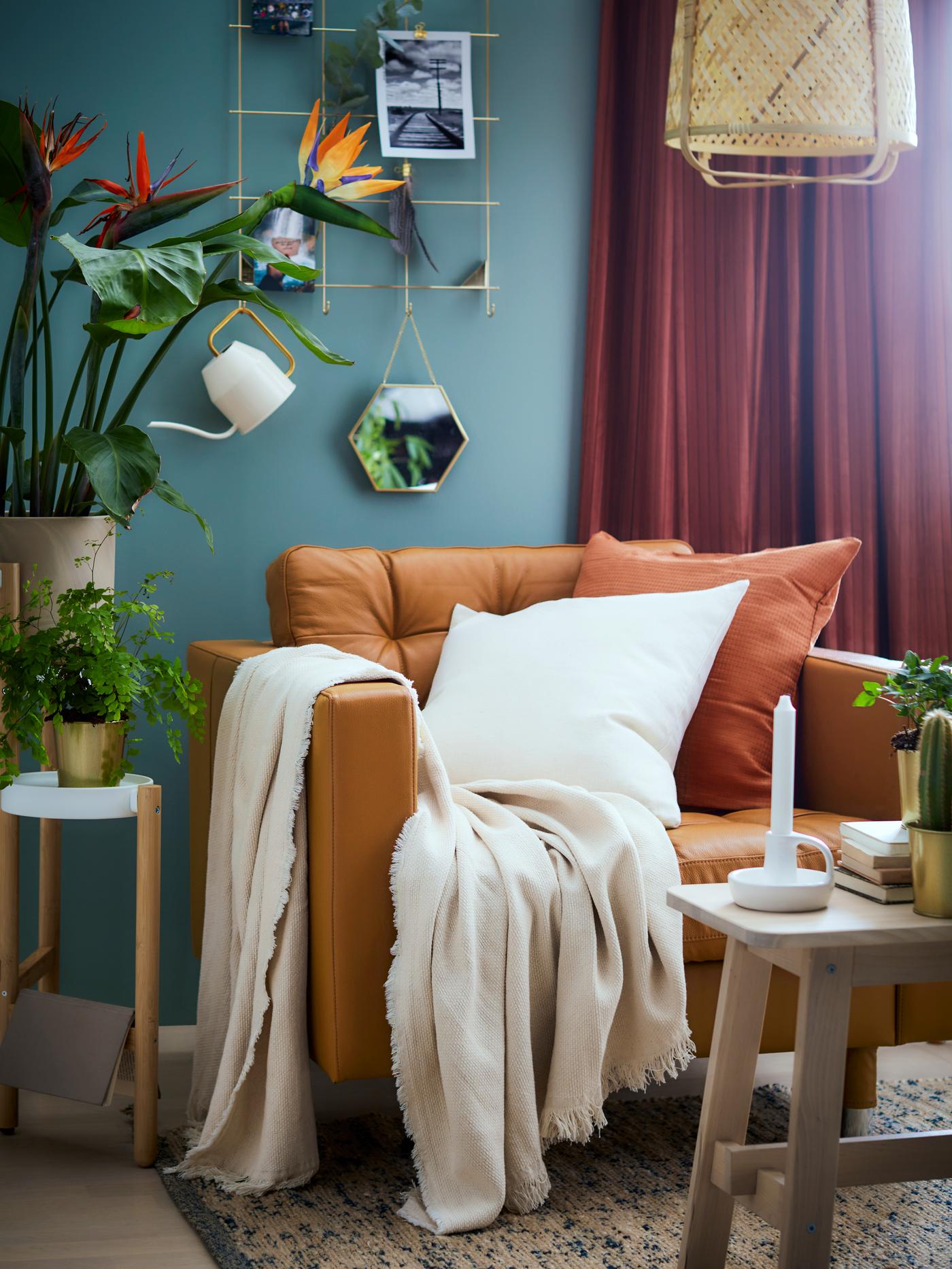 Sillón naranja LANDSKRONA con cojines naranjos y blancos y una manta blanca encima. En un living con mesa de madera y cortinas burdeo.