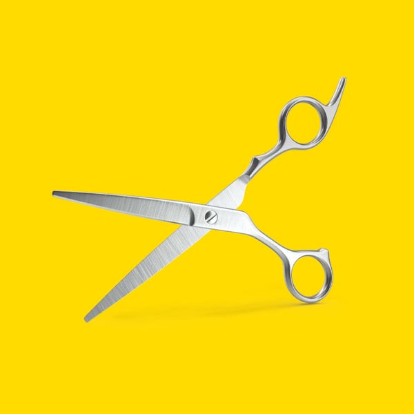 Silverfärgad frisörsax med två öglor, mot gul bakgrund.