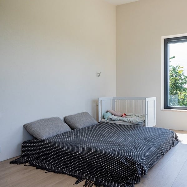 Simple Scandinavian bedroom with floor mattress, neutral walls, and baby crib