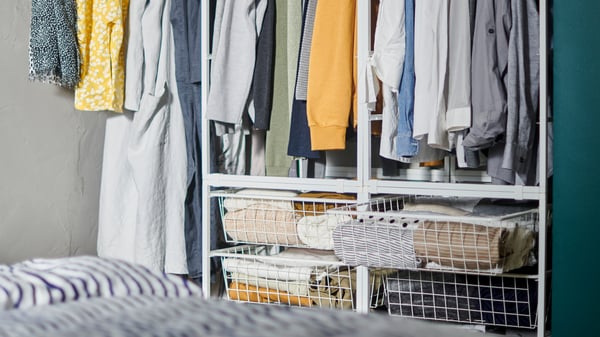 Sistema d’emmagatzematge JONAXEL amb cistelles metàl·liques i roba penjada i plegada de manera ordenada.